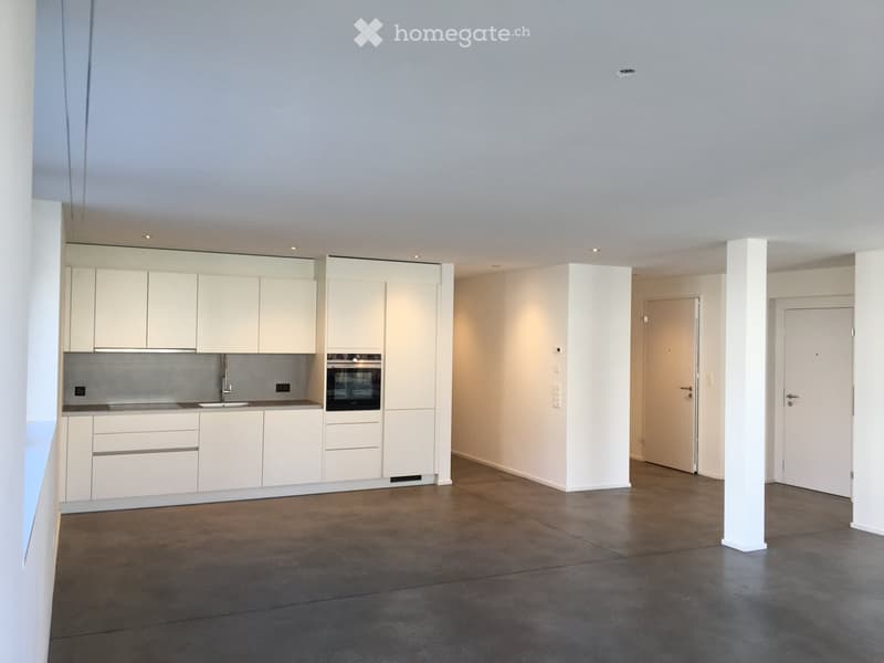 Empty room, white walls, white cabinets, concrete floor, kitchen area with sink, oven, and countertop