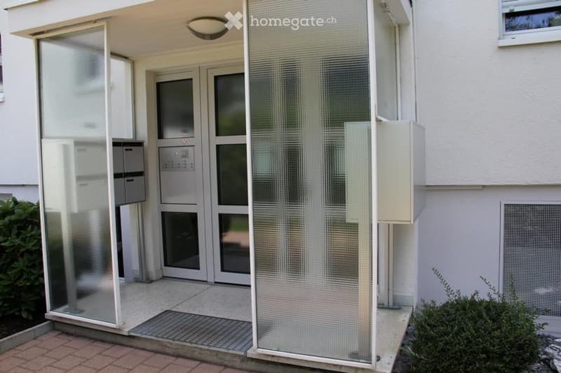 Entrance area of a building with glass doors, mailboxes, and a small covered porch.