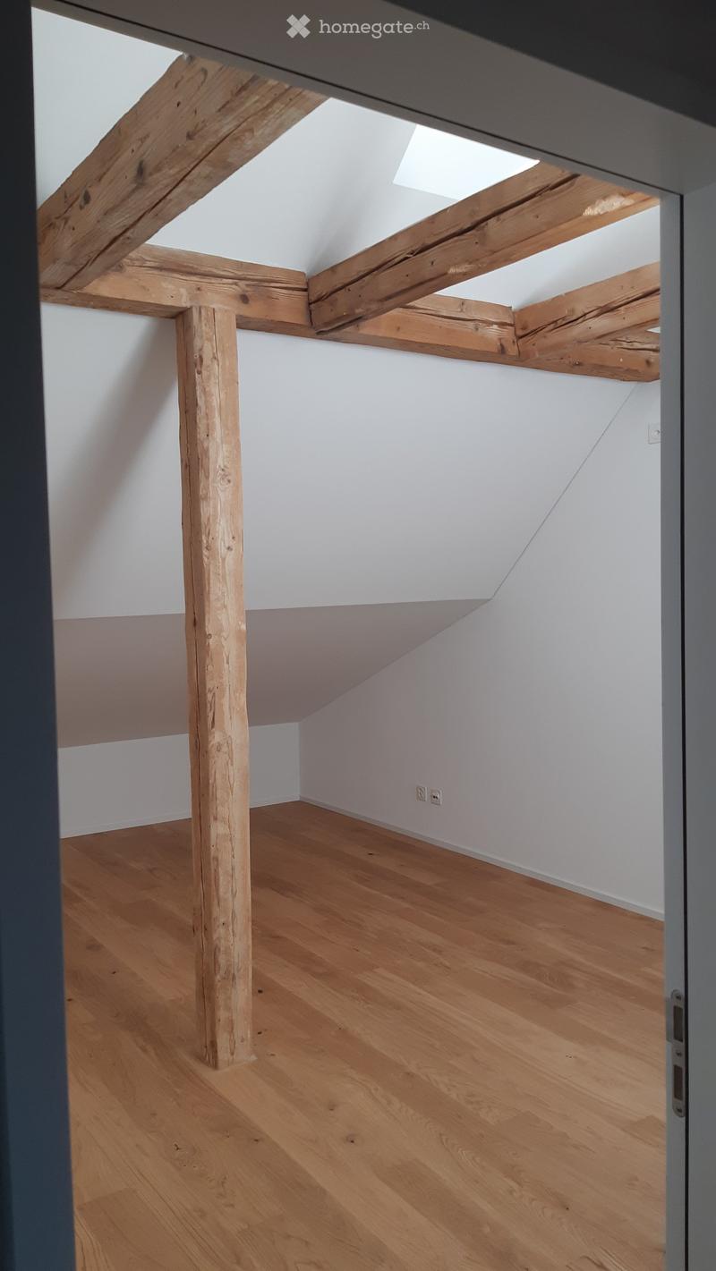 Empty attic space with wooden beams, wooden floor, and white walls. No furniture or equipment present.