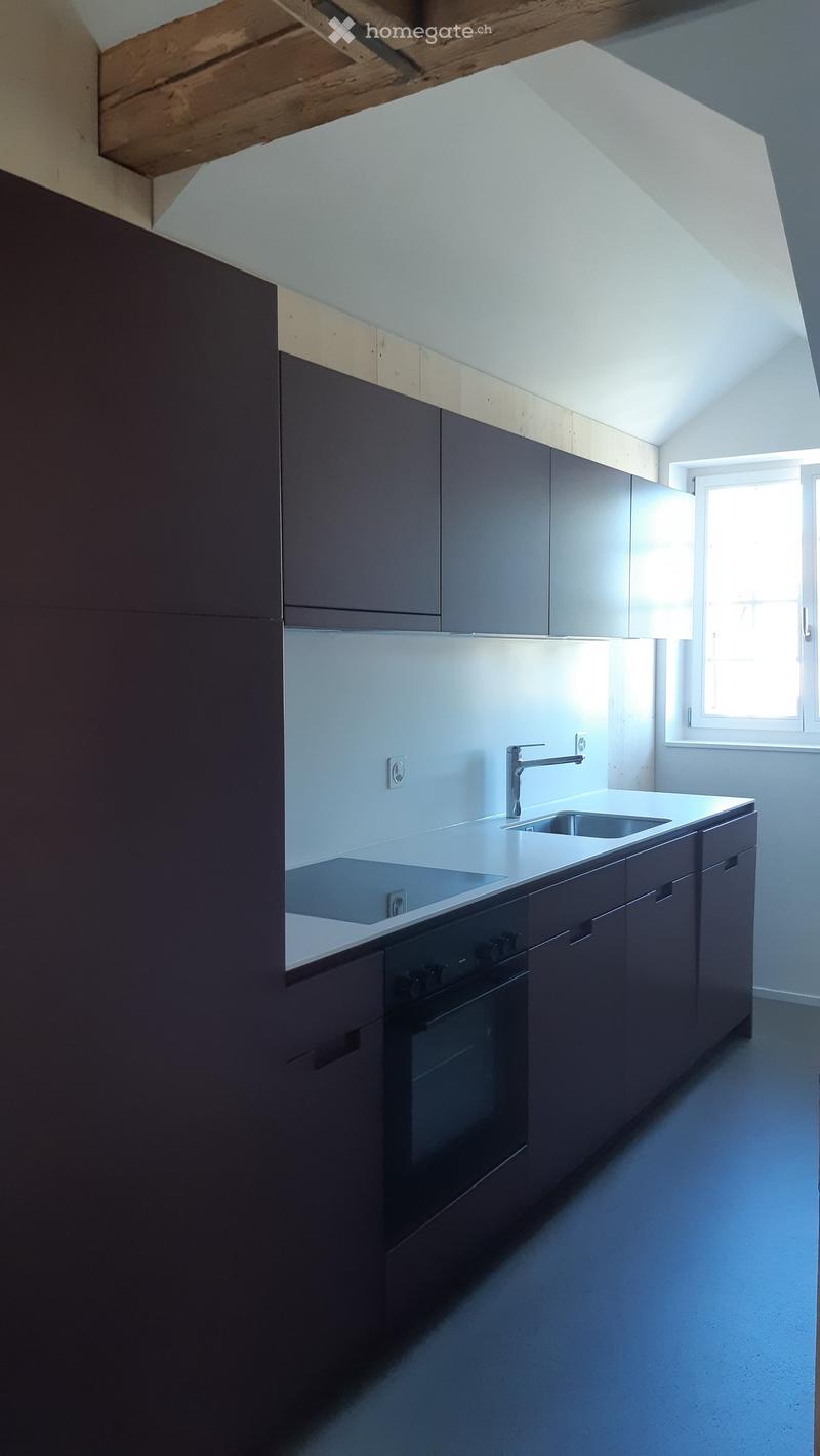 Modern kitchen with dark grey cabinets, white countertops, a sink, and an oven. The space features a skylight window and sleek, contemporary design.