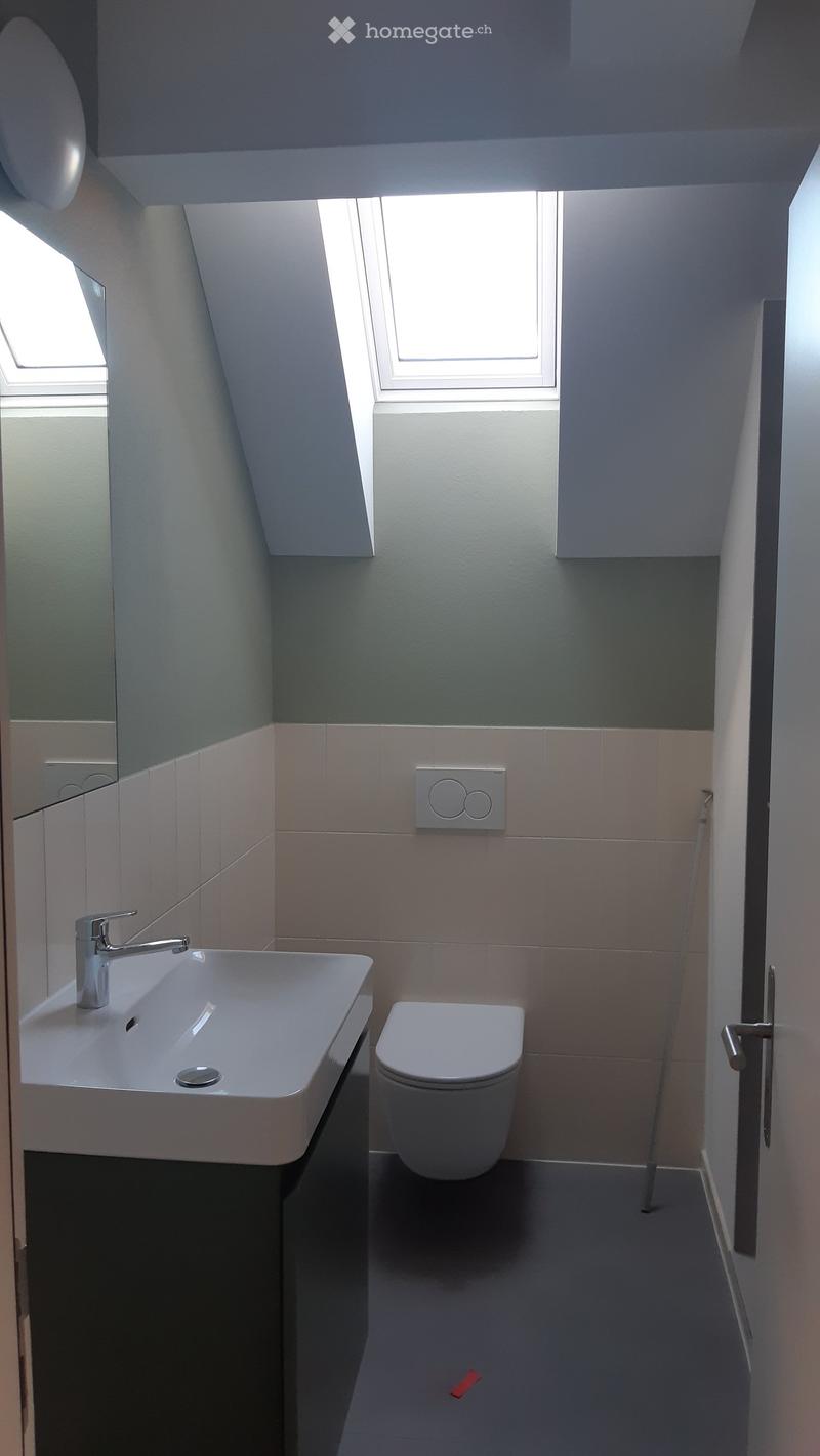 Modern bathroom with a white sink, chrome faucet, and toilet. Light grey tiles and a sleek design.