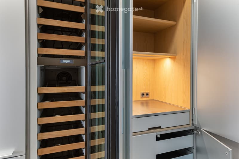 Modern kitchen with a built-in wine rack featuring wooden shelves and glass doors, adjacent to a cabinet with wooden shelves and a drawer.