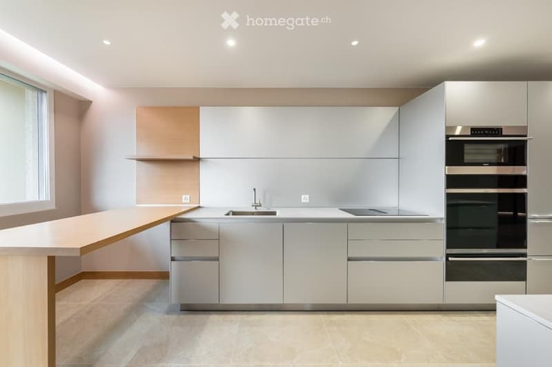 Modern kitchen with white and grey cabinets, a central island, stainless steel appliances, and a large window.