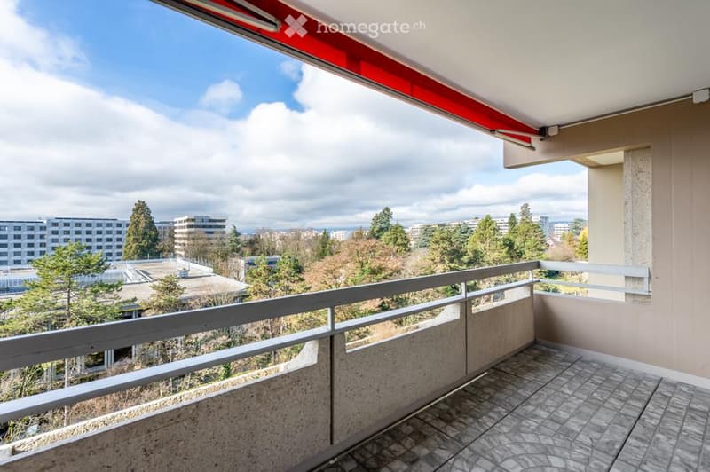Balcony with tiled floor, white railing, and a view of a cityscape with trees and buildings.