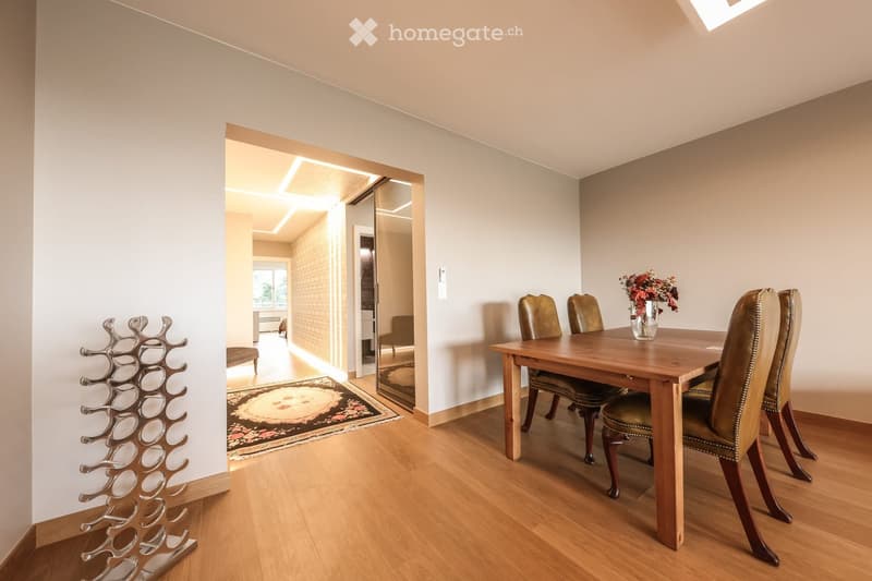 Dining room with wooden floor, dining table, four chairs, vase with flowers, mirror, and decorative shelf.