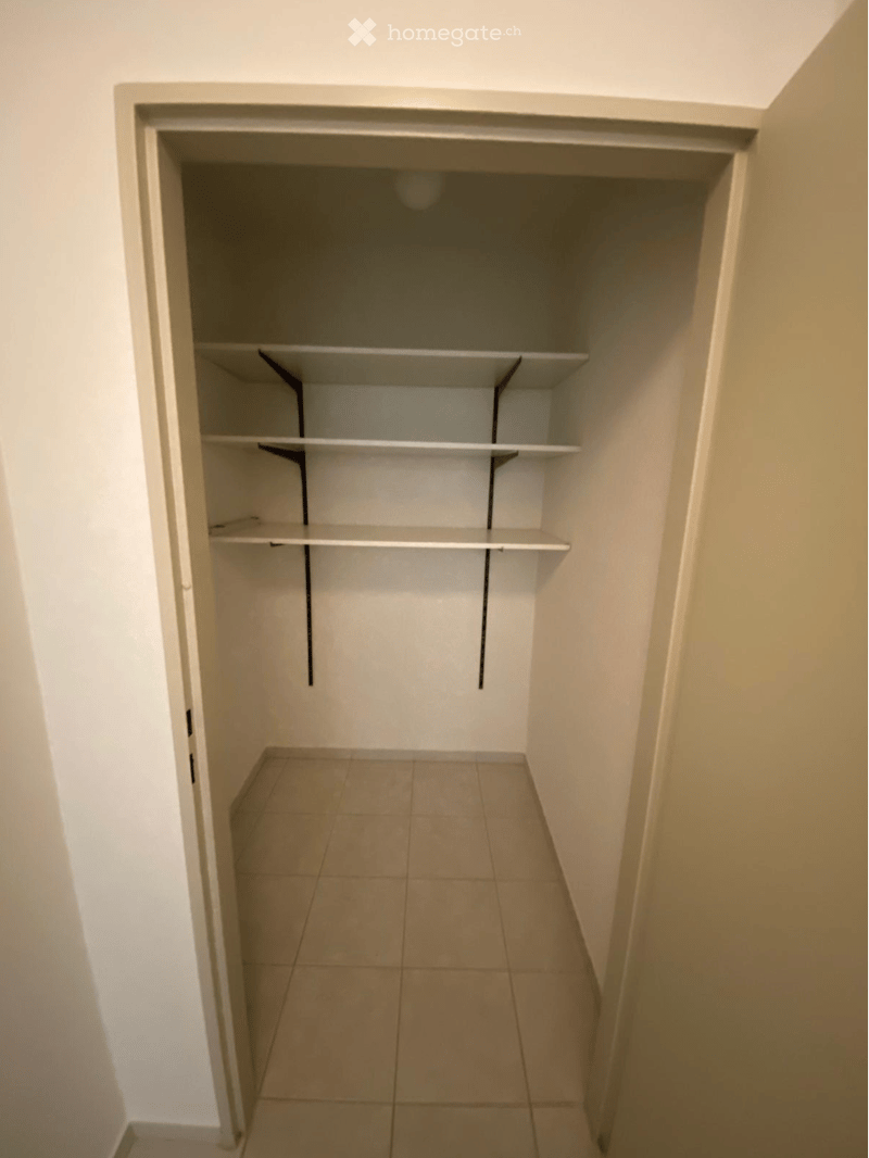 Empty closet with white walls, tiled floor, and built-in shelves.