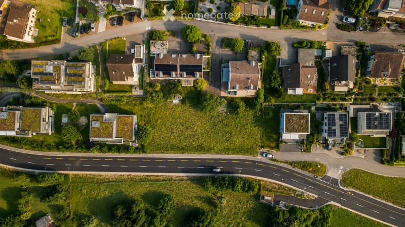 Aerial view of a residential neighborhood with multiple houses, solar panels on rooftops, and surrounding greenery.