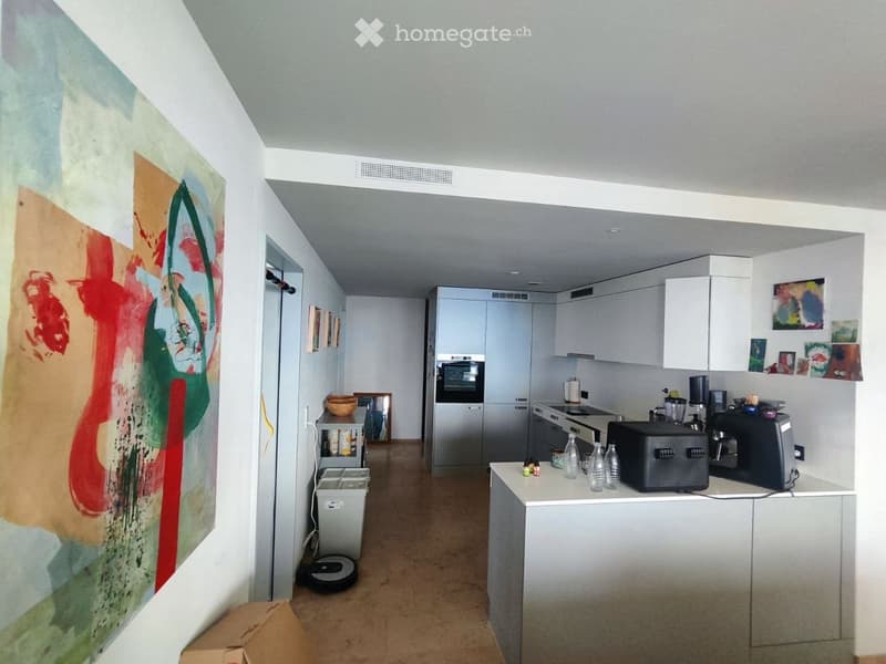 Modern kitchen with white cabinets, stainless steel appliances, and a central island. The space features a large abstract painting on one wall and several decorative items on shelves.