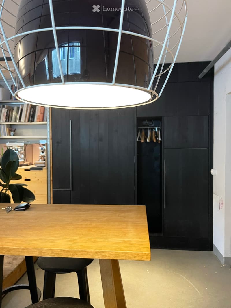 A modern, well-lit hallway with a large pendant light, a wooden table with a chair, a bookshelf, and a plant in the corner.