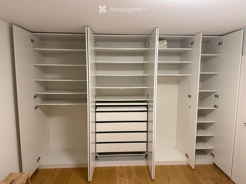 Empty room with wooden flooring and large white built-in storage unit with shelves and drawers.