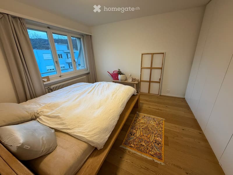 Cozy bedroom with a wooden bed, nightstand, decorative items, and a patterned rug on the floor.