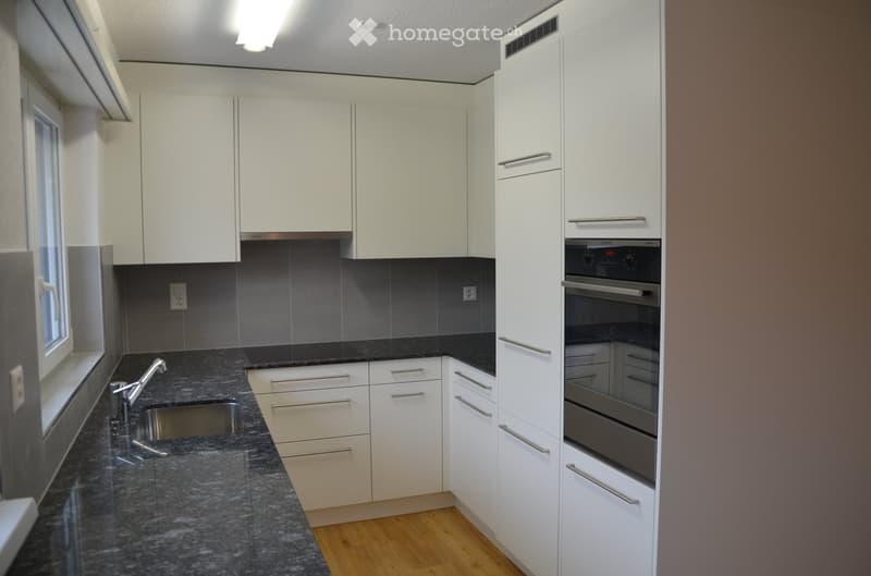 Modern kitchen with white cabinets, granite countertops, stainless steel sink and faucet, and built-in oven.