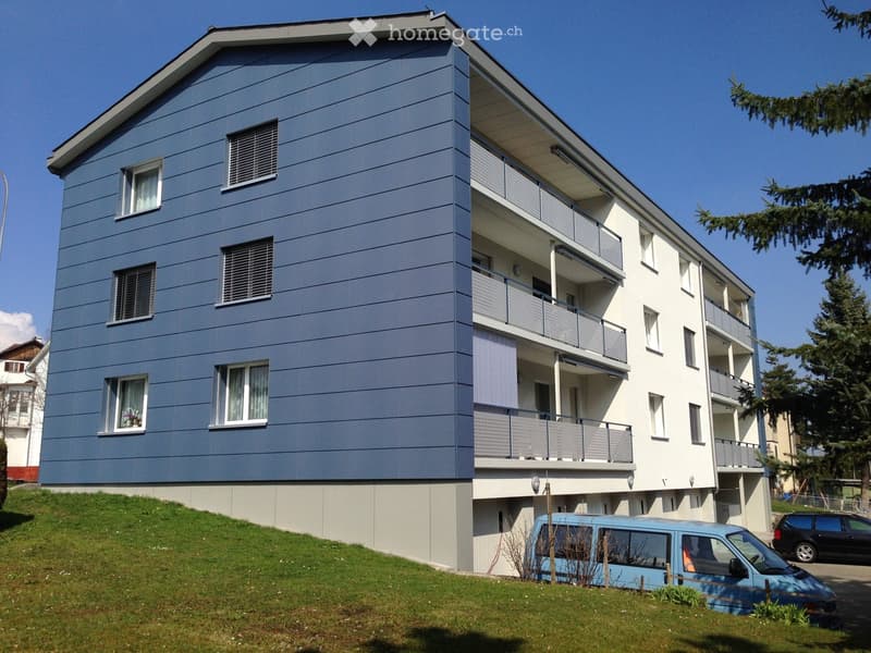 Modern two-story apartment building with blue and white exterior, multiple balconies, and a raised ground floor.