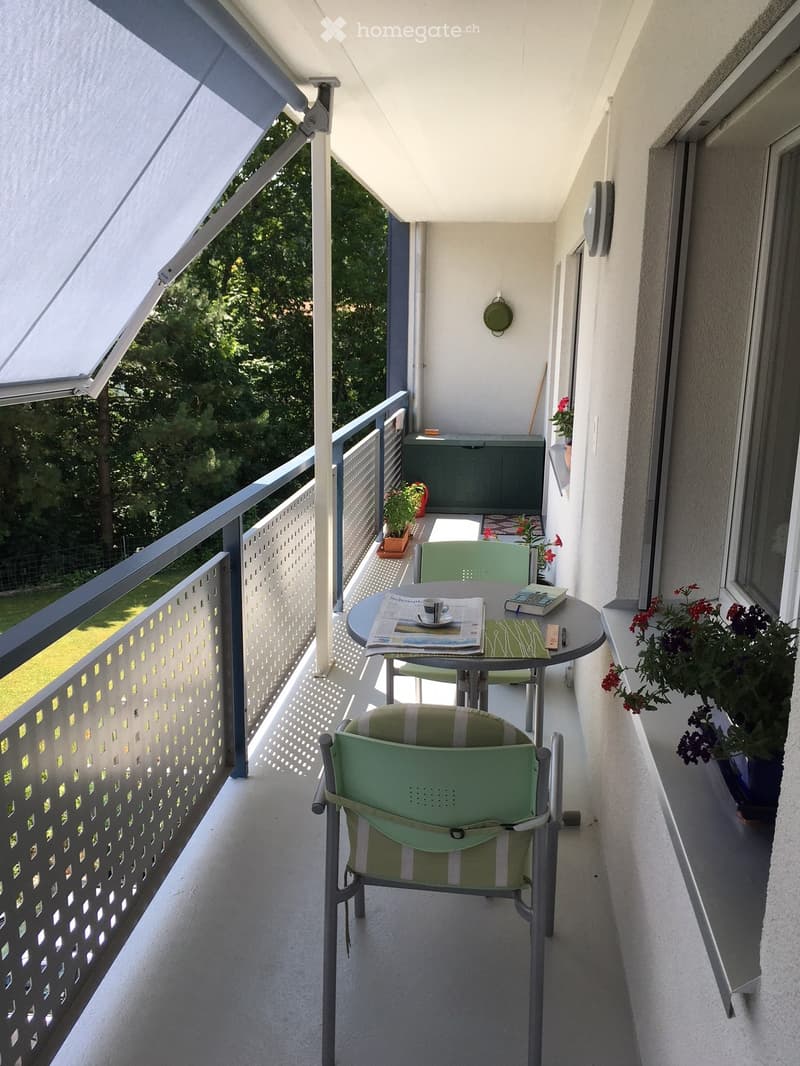 Balcony with a round table, two green chairs, a cup, a book, and flower pots.