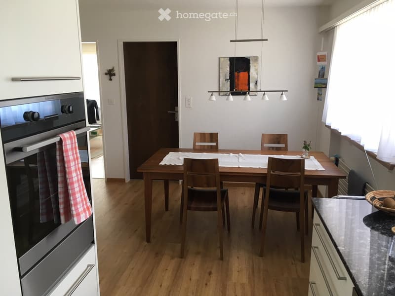 Modern kitchen with wooden dining table, six chairs, built-in oven, and countertop with a decorative bowl.