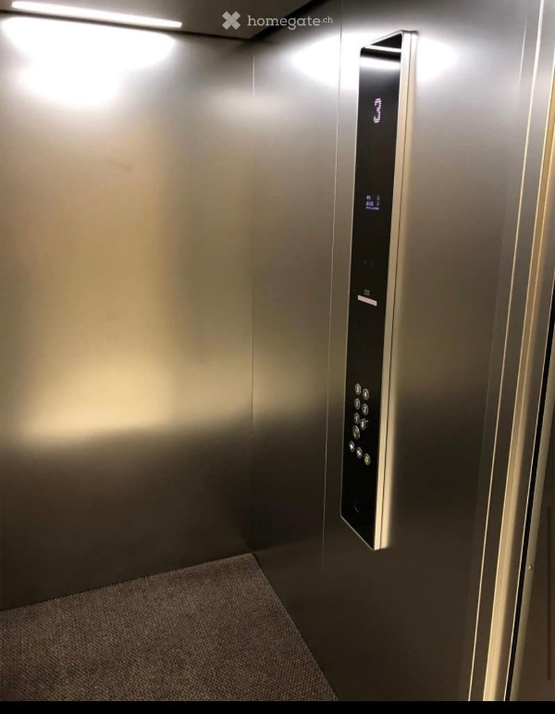 Modern elevator interior with stainless steel walls, digital display panel, and carpeted floor.