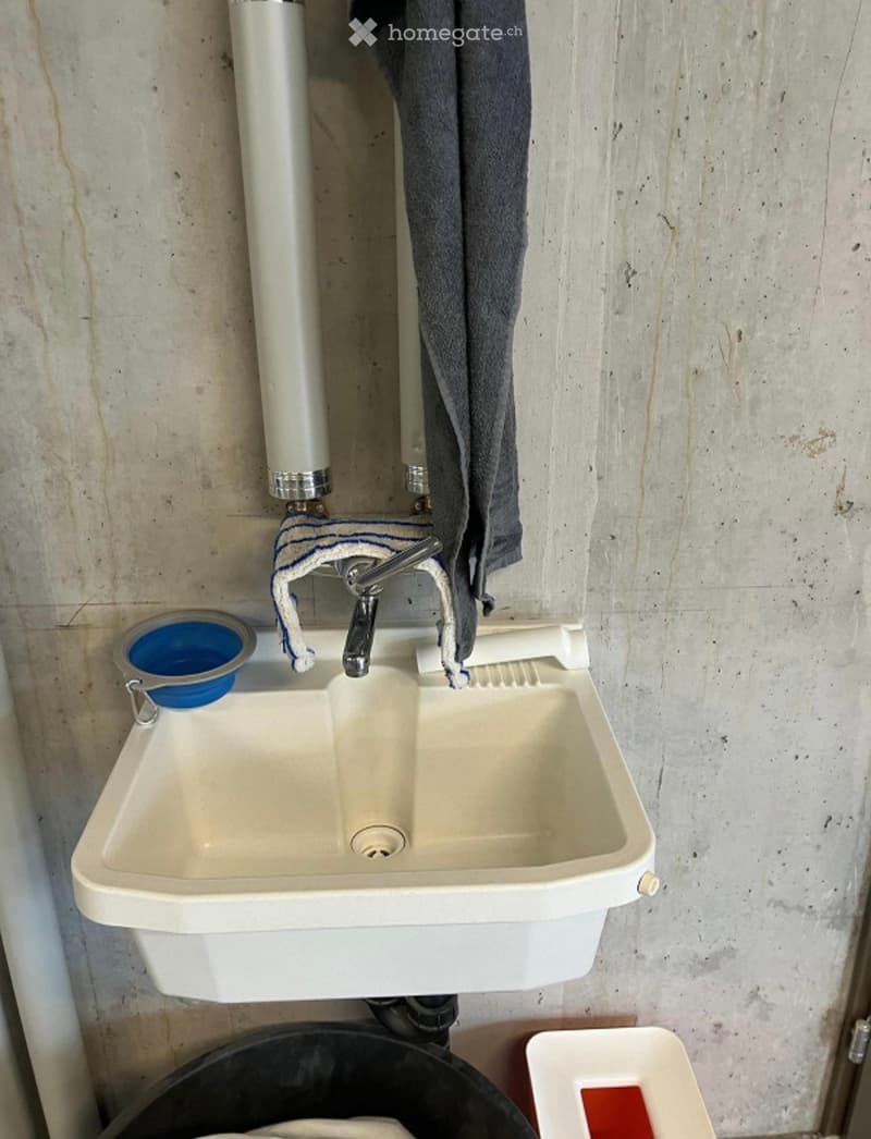 A simple bathroom sink with a faucet, a towel hanging on the wall, and a blue cup on the left side.