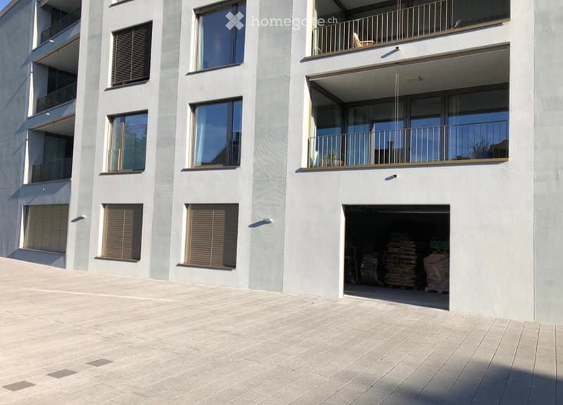 Modern multi-story building with balconies, large windows, and a visible garage entrance.