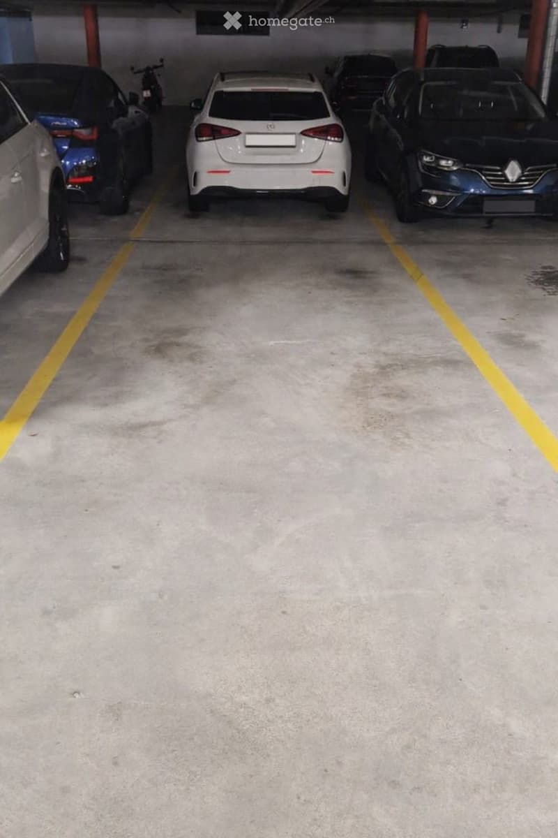 Underground parking area with several parked cars, including a white sedan, a black SUV, and a motorcycle, marked with yellow lines.