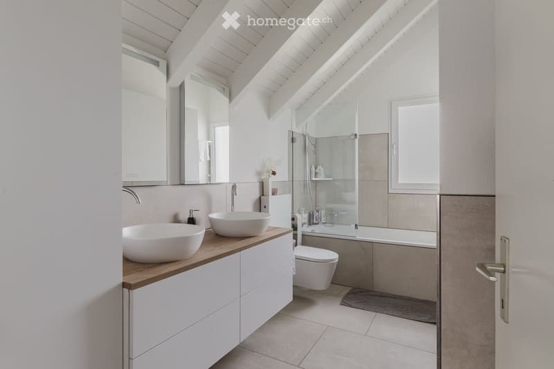 Modern bathroom with a sleek white sink, mirror, toilet, bathtub, and glass-enclosed shower. The space features a wooden countertop and white cabinets.