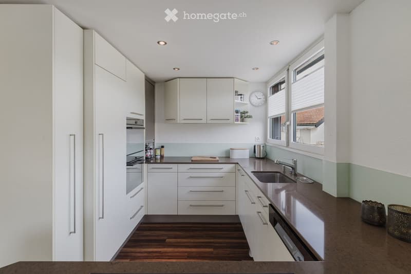 Modern kitchen with white cabinets, dark countertops, and stainless steel appliances. Features include a built-in oven, refrigerator, sink, and a clock on the wall.