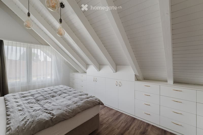 A modern attic bedroom with wooden slanted ceilings, white built-in wardrobes, a bed with a fur throw, and pendant lights.