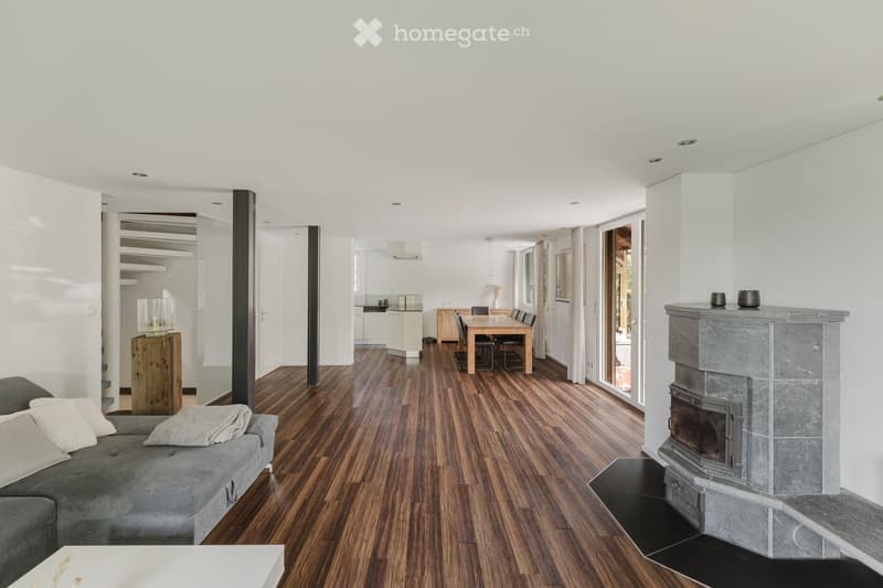 Modern living room with hardwood flooring, grey sofa, coffee table, fireplace, dining area with table and chairs, and open-plan layout with visible kitchen area.