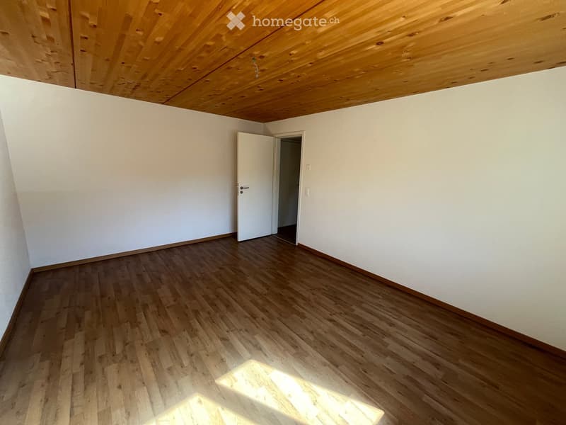 Empty room with wooden flooring and white walls, featuring a wooden ceiling and a doorway leading to another space.