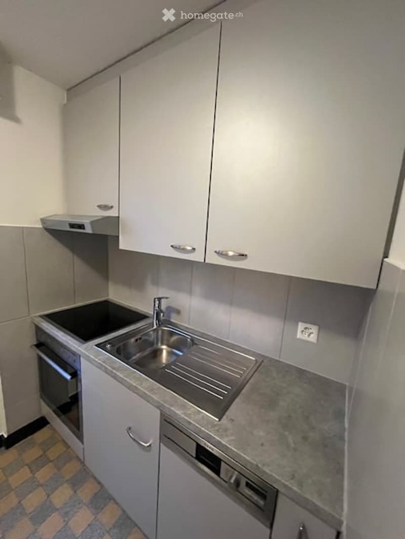 Modern kitchen with white cabinets, stainless steel sink, oven, and dishwasher. Countertop has a marble finish, and the floor is tiled.