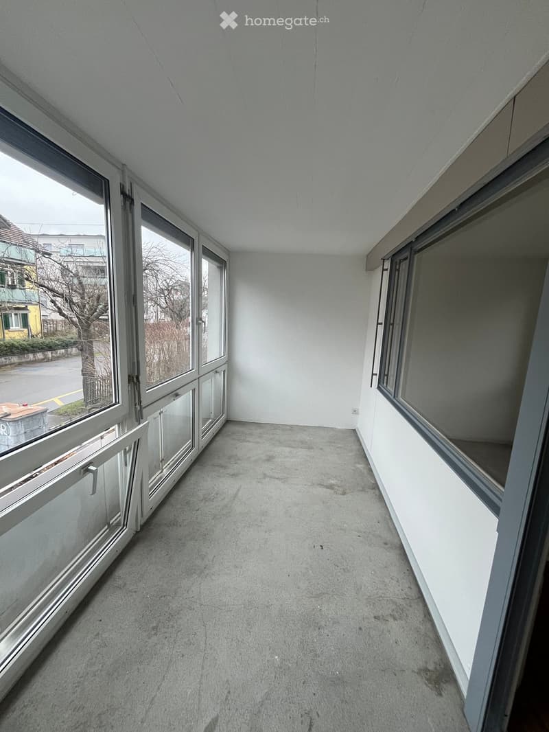 Empty balcony with concrete floor, large windows, and metal frames.