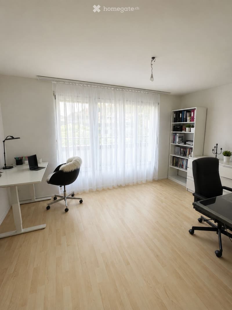 Bright, modern office with light wooden flooring, large window with white curtains, white desk with laptop and chair, bookshelf with books and decorative items, and a hanging light fixture.