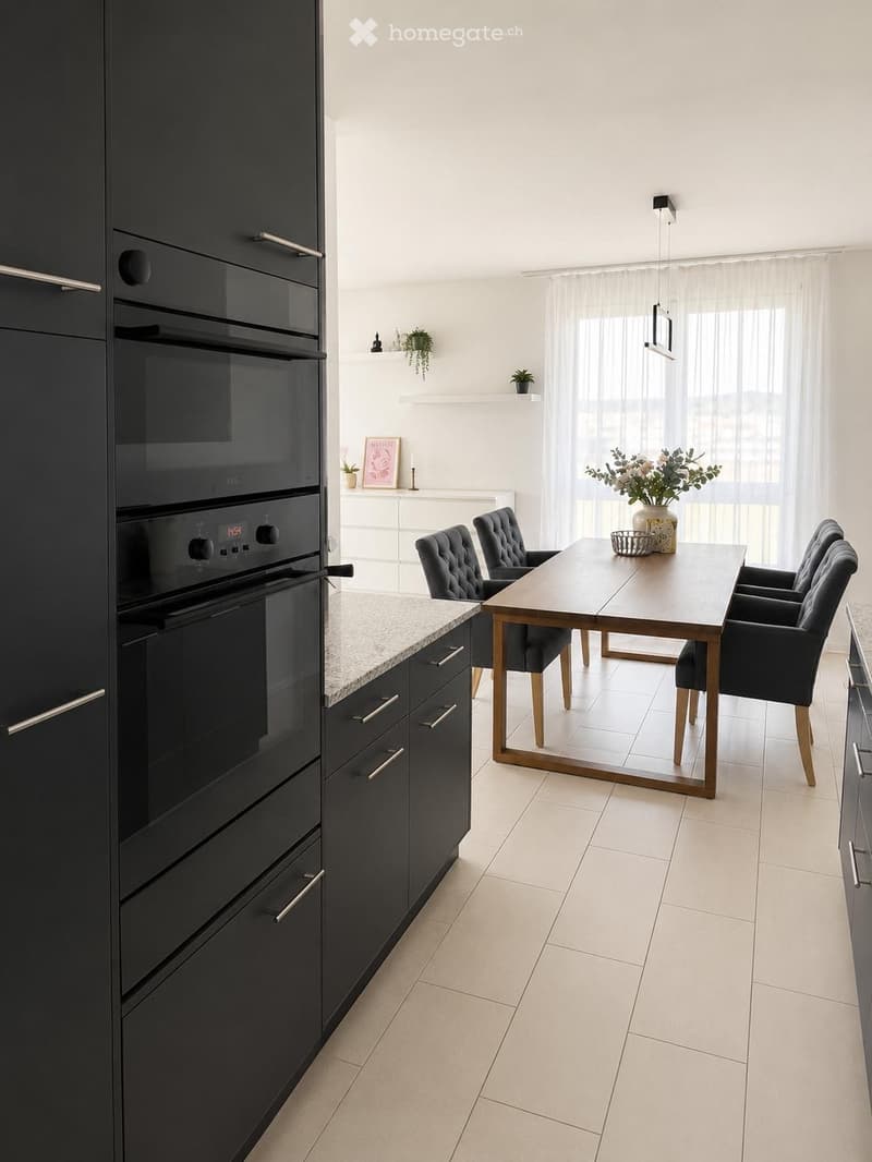 Modern kitchen with dark cabinets, a built-in oven, a dining table with chairs, and decorative items on shelves and the table.
