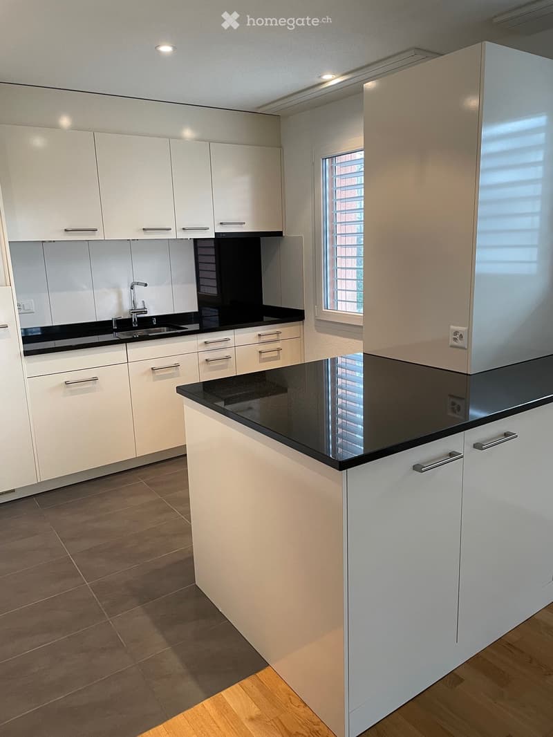Modern kitchen with white cabinets, black countertops, and a central island. Features a sink with a modern faucet and ample storage space.