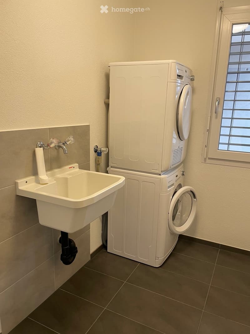 Bathroom with a white sink, faucet, and a stacked washing machine and dryer unit.