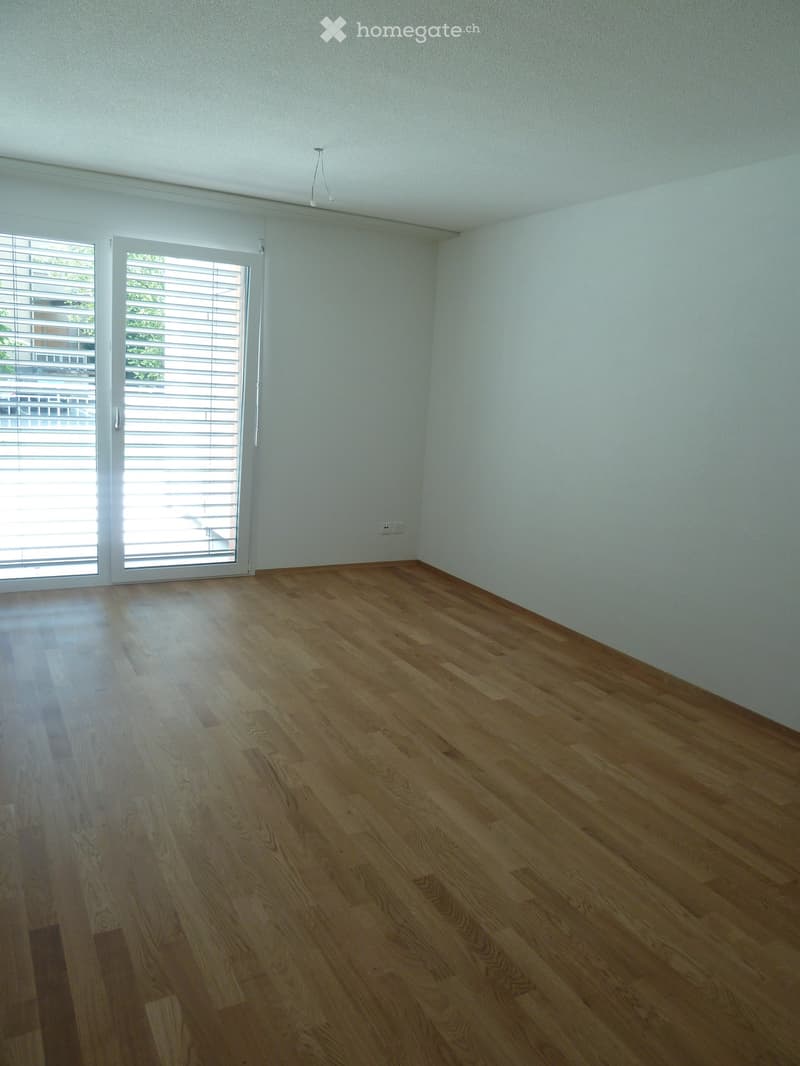 Empty room with light-colored wooden flooring, white walls, and large sliding glass doors with blinds.