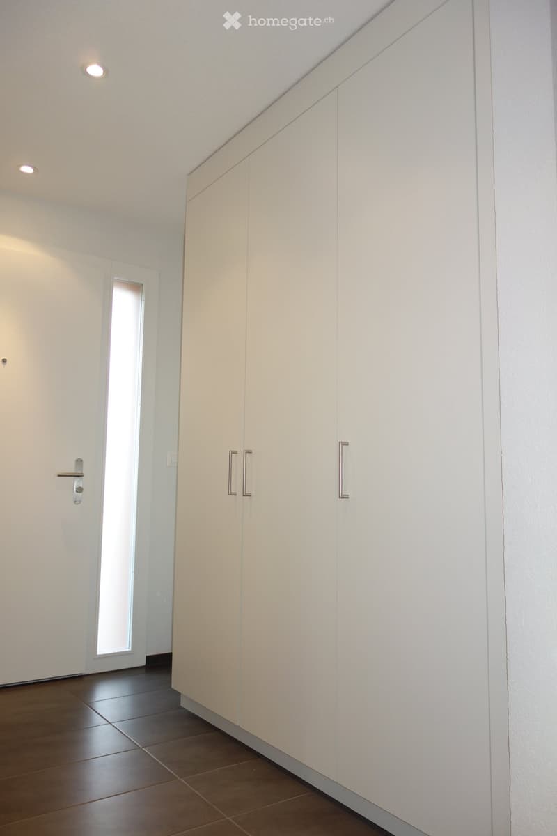 Modern hallway with white walls, tiled floor, built-in white cabinets, and recessed lighting.