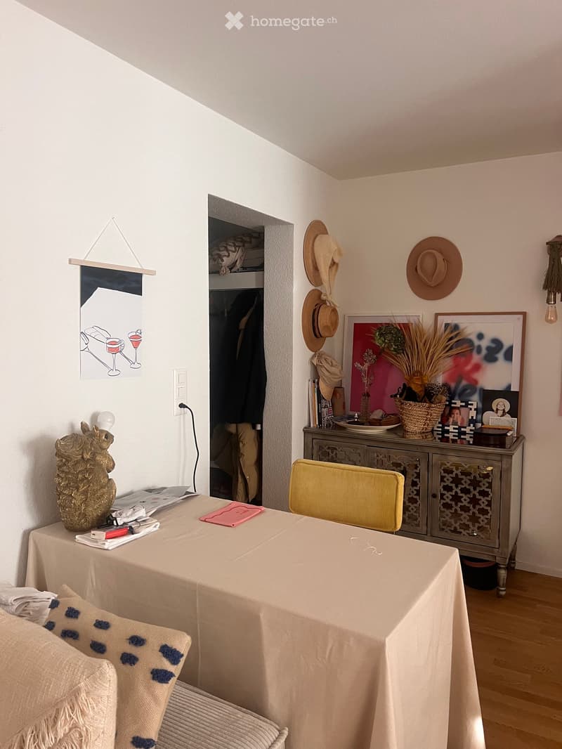 A cozy, well-decorated room with a sofa, a small table, a cabinet, and various decorative items including hats, a basket, and a sculpture.