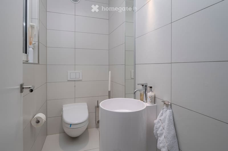 Modern bathroom with white tiles, a toilet, a sink with a modern faucet, a towel, a mirror, and a candle on the sink counter.