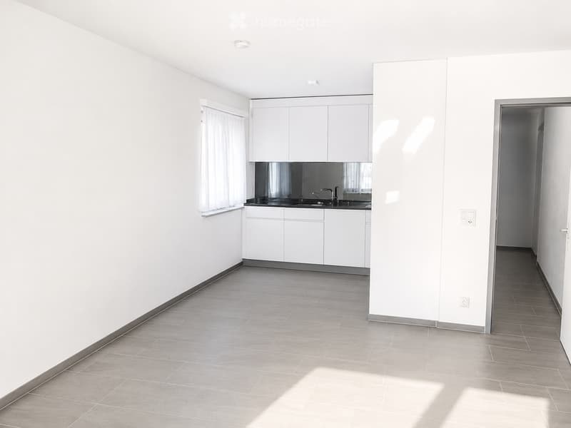 Empty kitchen with white cabinets, a sink, and tiled flooring. The space is clean and unfurnished, with no visible appliances or furniture.