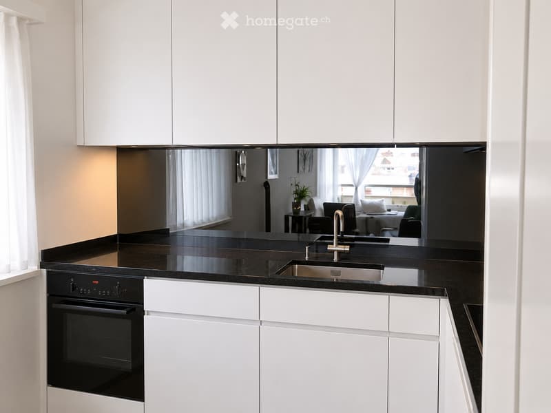 Modern kitchen with white cabinets, black countertops, stainless steel sink, and built-in oven.