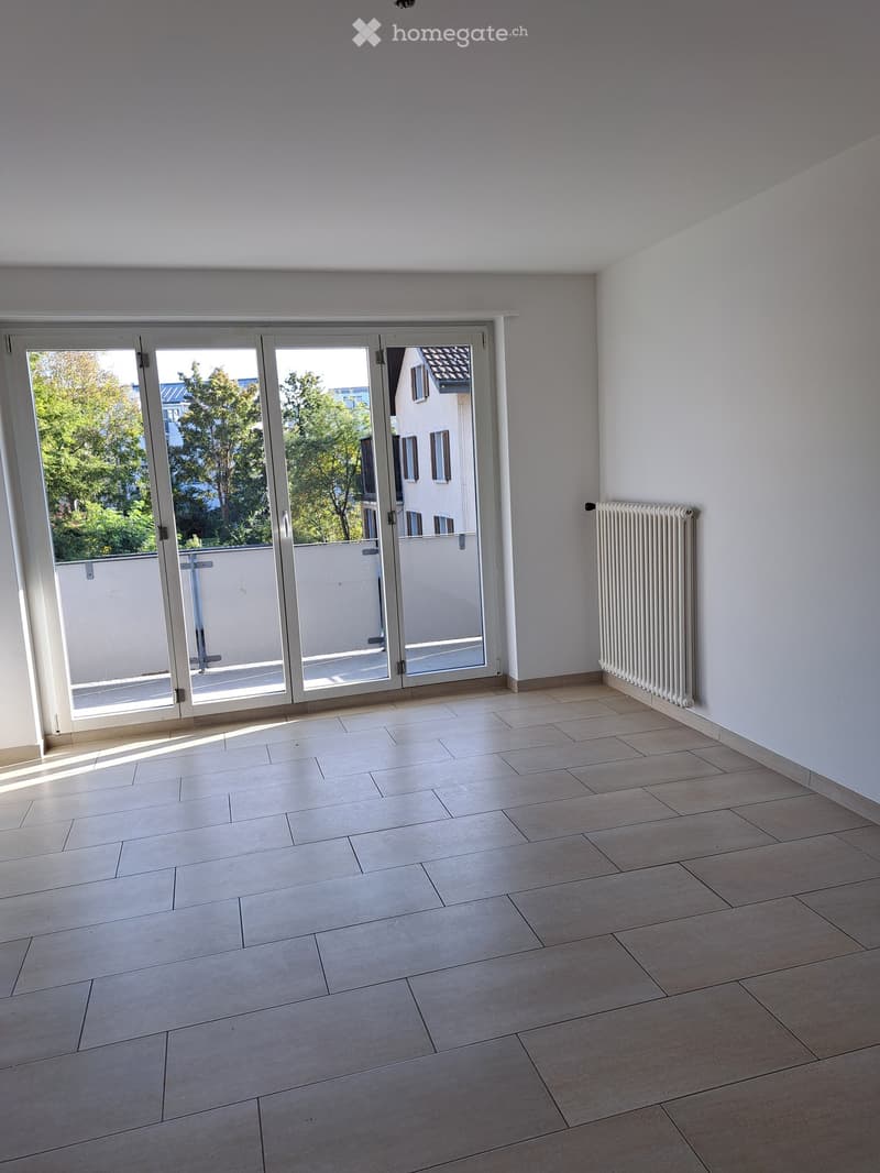 Empty room with tiled floor, white walls, large sliding glass doors leading to a balcony, and a radiator on one wall.