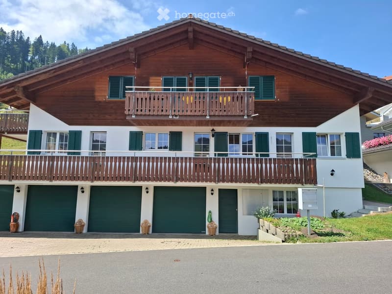 Two-story wooden house with green shutters, balconies, and multiple garage doors.