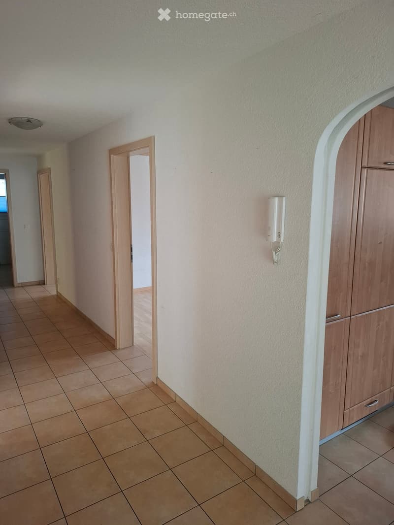 Empty hallway with tiled floor, beige walls, wooden doors, and a wall-mounted intercom system.