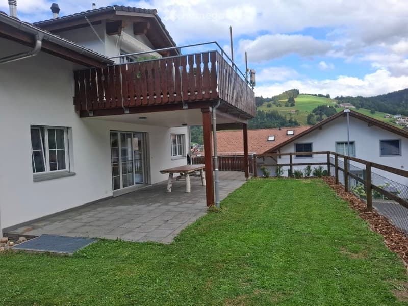 A well-maintained garden area with a wooden bench, a paved patio, and a scenic view of rolling hills and distant houses.