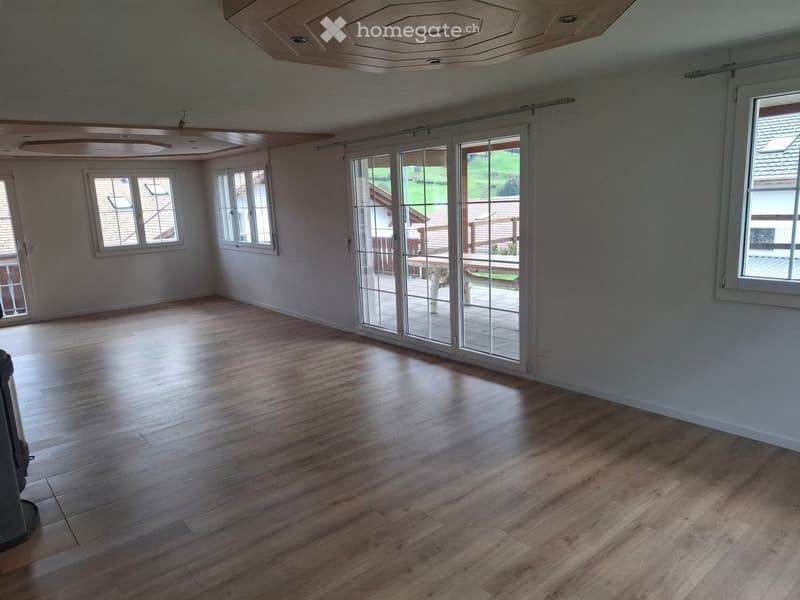 Empty room with wooden flooring, large windows, and sliding glass doors leading to an outdoor area.