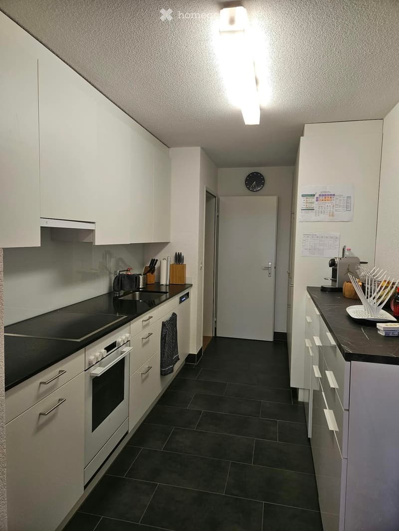Modern kitchen with white cabinets, black countertops, induction stove, oven, and various appliances.