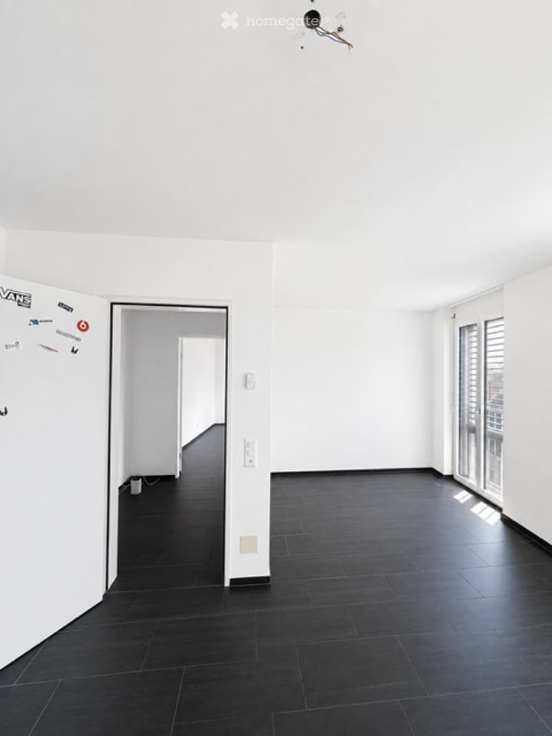 Completely empty room with white walls, black tiled floor, and large windows with blinds. No furniture or equipment.