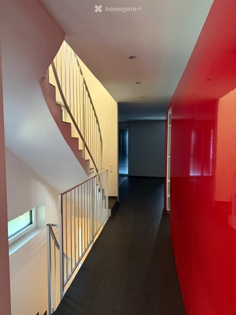 Modern hallway with red and white walls, dark flooring, and a staircase with a metal railing on the left side.