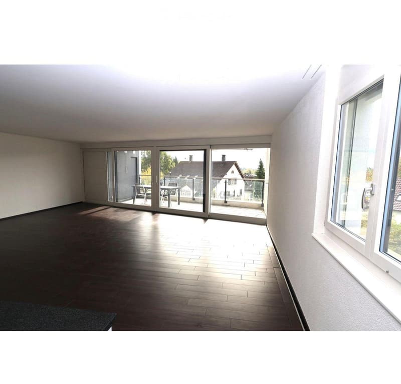Empty room with wooden flooring, large sliding glass doors leading to a balcony, and white walls.