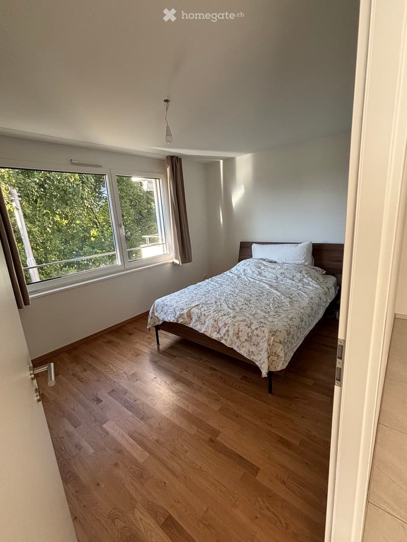 Bedroom with wooden flooring, a bed with a patterned duvet, and a window with curtains.